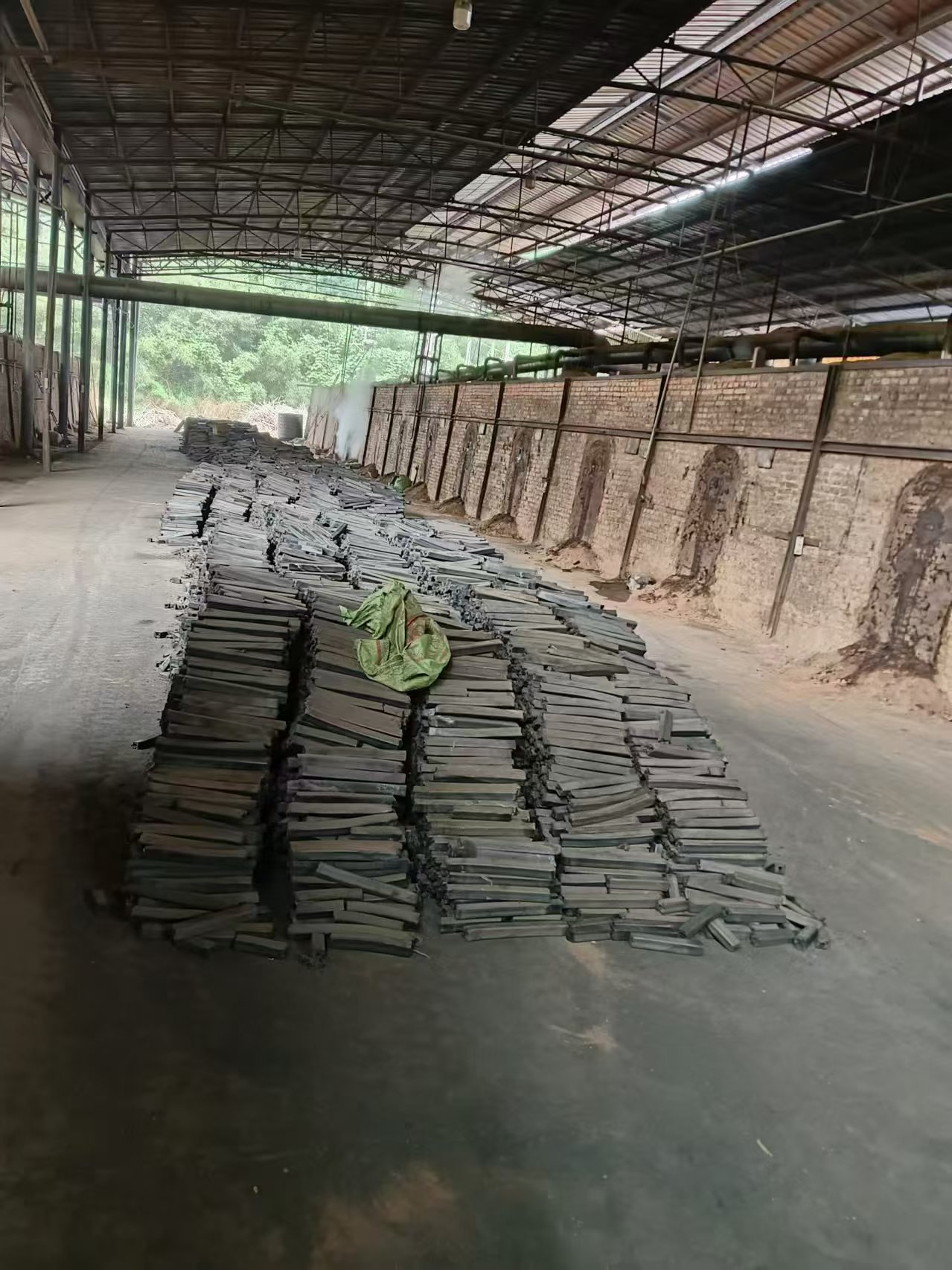 Carbonization hall with a row of brick kilns and stacks of finished charcoal bars on the floor